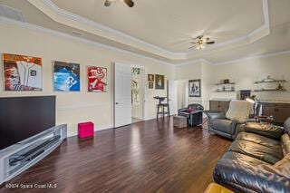 living room with dark hardwood / wood-style floors, ceiling fan, a raised ceiling, and ornamental molding