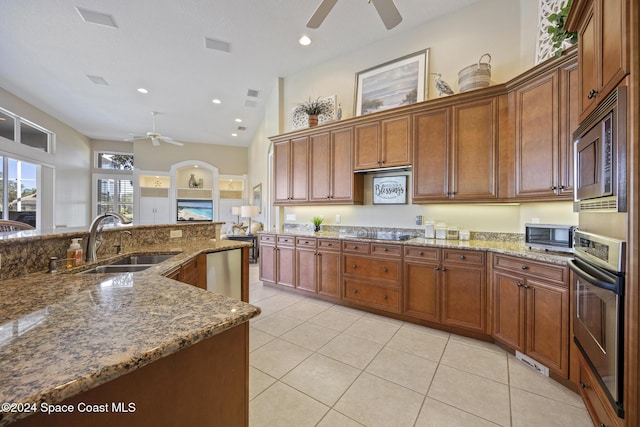 kitchen featuring sink, ceiling fan, dark stone countertops, light tile patterned flooring, and stainless steel appliances