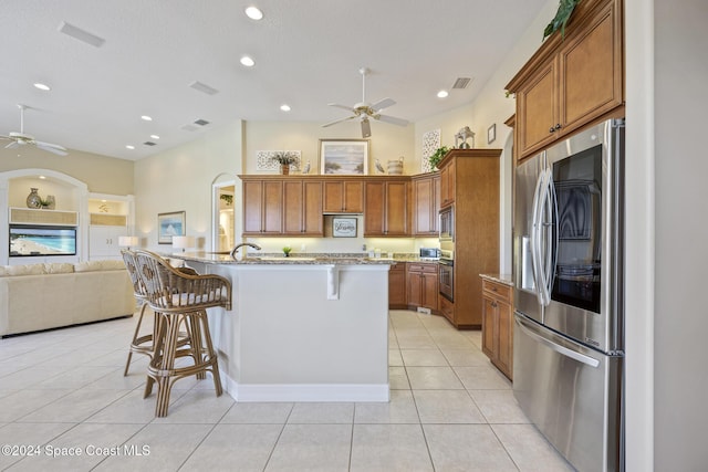 kitchen featuring light stone countertops, a kitchen breakfast bar, stainless steel appliances, a kitchen island with sink, and light tile patterned floors