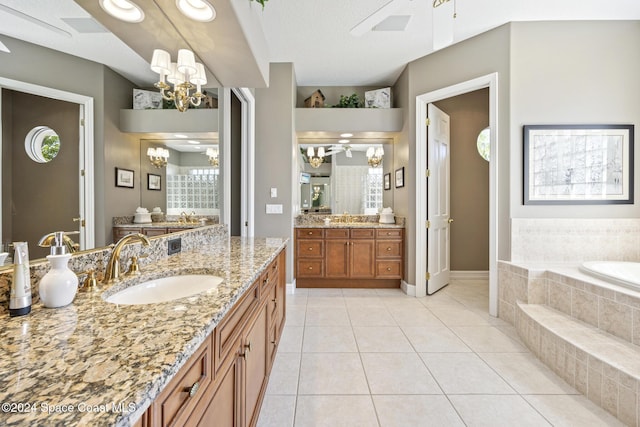 bathroom with tiled tub, tile patterned flooring, vanity, and ceiling fan with notable chandelier