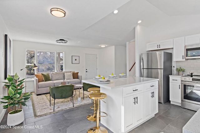 kitchen featuring white cabinetry, backsplash, a kitchen bar, a kitchen island, and appliances with stainless steel finishes