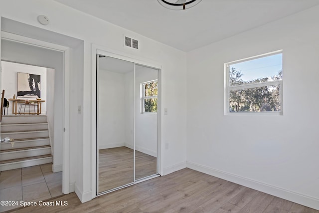 unfurnished bedroom featuring multiple windows, a closet, and light wood-type flooring