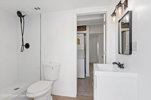 bathroom featuring hardwood / wood-style floors, tiled shower, toilet, vanity, and stacked washer and clothes dryer