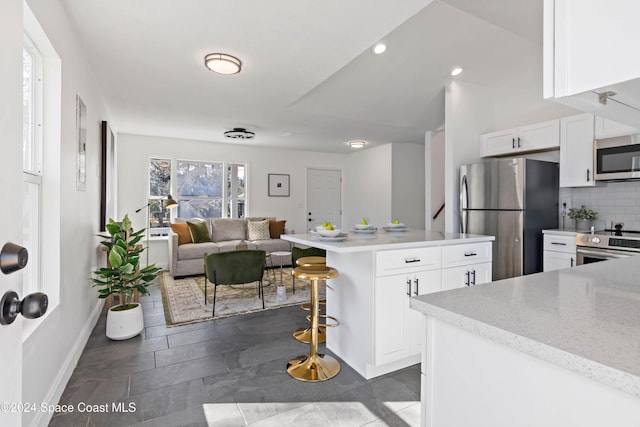 kitchen with decorative backsplash, light stone counters, a breakfast bar, stainless steel appliances, and white cabinets