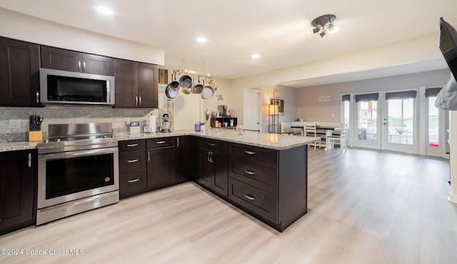 kitchen with kitchen peninsula, light wood-type flooring, backsplash, dark brown cabinetry, and stainless steel appliances