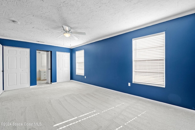 unfurnished bedroom featuring multiple closets, ceiling fan, crown molding, light colored carpet, and a textured ceiling