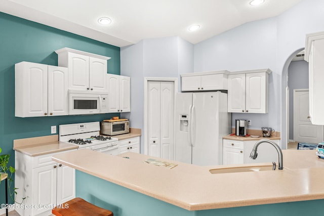 kitchen with white appliances, white cabinets, a kitchen bar, and sink