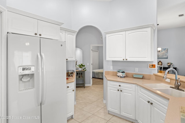 kitchen featuring white refrigerator with ice dispenser, white cabinetry, light tile patterned floors, and sink