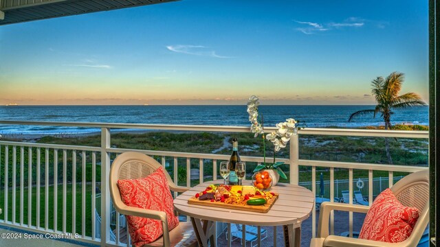 balcony at dusk featuring a beach view and a water view