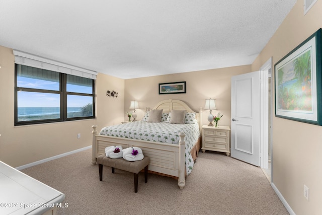 bedroom featuring a water view, light colored carpet, and a textured ceiling