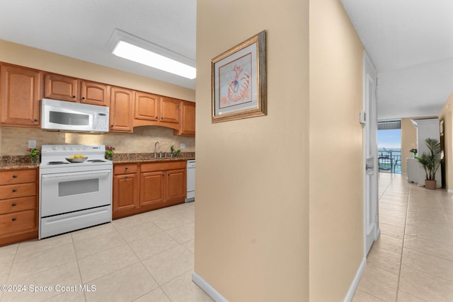 kitchen featuring sink, light tile patterned floors, stone countertops, and white appliances