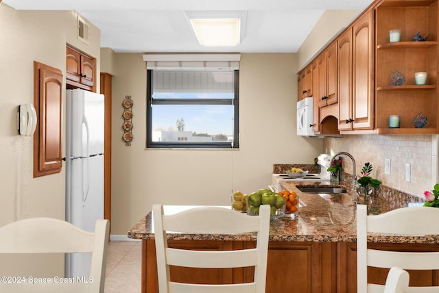 kitchen featuring kitchen peninsula, backsplash, dark stone counters, white appliances, and light tile patterned floors