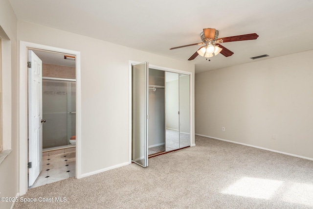 unfurnished bedroom with a closet, light colored carpet, ensuite bath, and ceiling fan