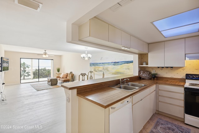 kitchen with white appliances, wooden counters, ceiling fan with notable chandelier, sink, and kitchen peninsula