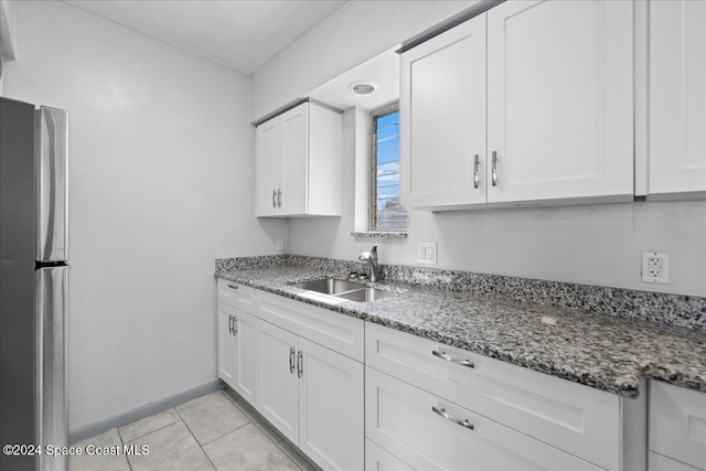 kitchen with white cabinets, stone countertops, stainless steel refrigerator, and sink