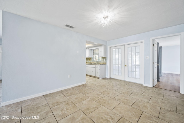 unfurnished living room featuring light tile patterned flooring, an inviting chandelier, sink, and french doors