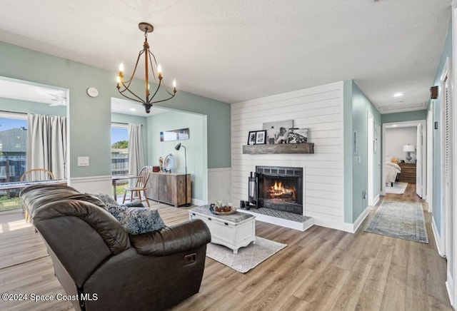 living room with a textured ceiling, a large fireplace, light hardwood / wood-style floors, and an inviting chandelier