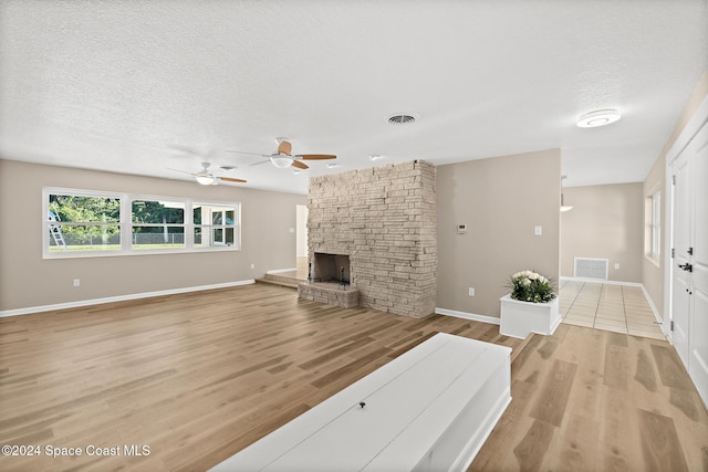 unfurnished living room featuring a fireplace, ceiling fan, light hardwood / wood-style flooring, and a textured ceiling