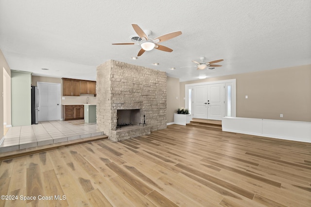 8303 Sylvan Dr, Melbourne, FL 32904 - unfurnished living room featuring a ceiling fan, light wood-style flooring, a stone fireplace, recessed lighting, and a textured ceiling