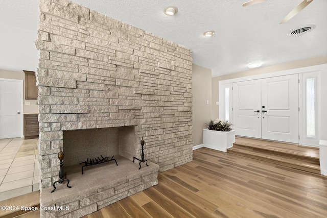 entryway with a stone fireplace, ceiling fan, hardwood / wood-style floors, and a textured ceiling