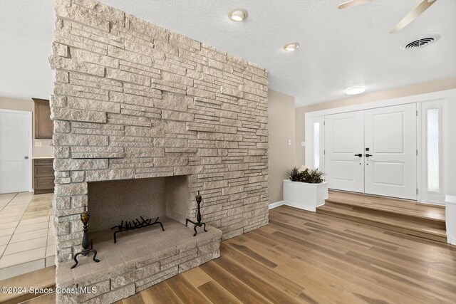 8303 Sylvan Dr, Melbourne, FL 32904 - foyer entrance featuring a stone fireplace, light wood-style flooring, a ceiling fan, and a textured ceiling