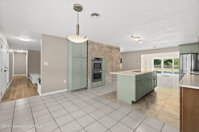 kitchen with appliances with stainless steel finishes, a textured ceiling, decorative light fixtures, green cabinets, and an island with sink