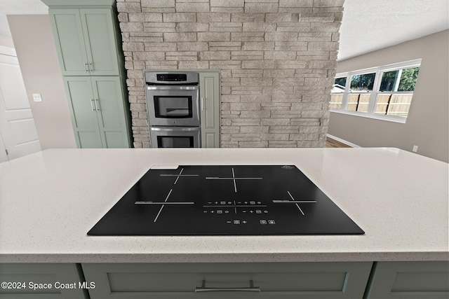 8303 Sylvan Dr, Melbourne, FL 32904 - kitchen featuring cooktop, stainless steel double oven, green cabinetry, and light stone counters