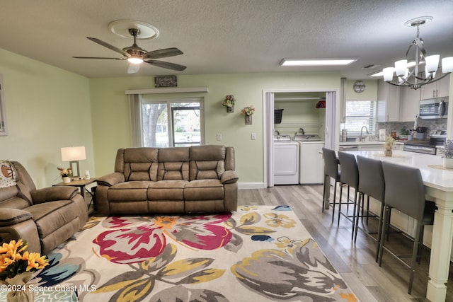 living room featuring sink, light hardwood / wood-style flooring, independent washer and dryer, a textured ceiling, and ceiling fan with notable chandelier