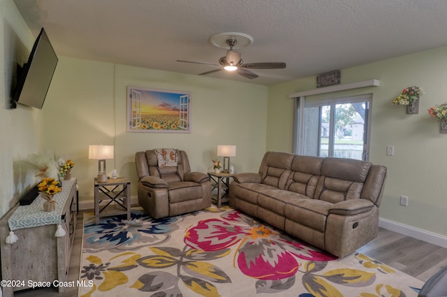 living room with ceiling fan, light wood-type flooring, and a textured ceiling