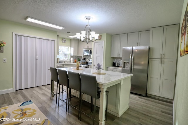 kitchen featuring light stone countertops, a center island, hanging light fixtures, stainless steel appliances, and light wood-type flooring