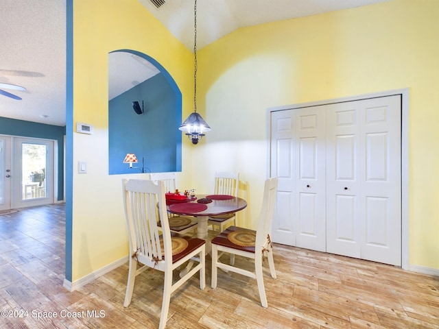 dining area with ceiling fan with notable chandelier, wood-type flooring, a textured ceiling, and vaulted ceiling