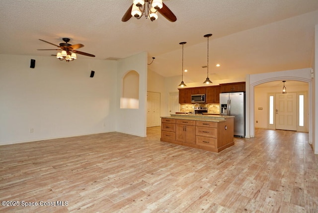 kitchen with lofted ceiling, decorative light fixtures, stainless steel appliances, backsplash, and a center island with sink