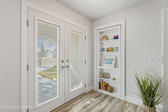 entryway with built in shelves, french doors, light hardwood / wood-style floors, and a textured ceiling