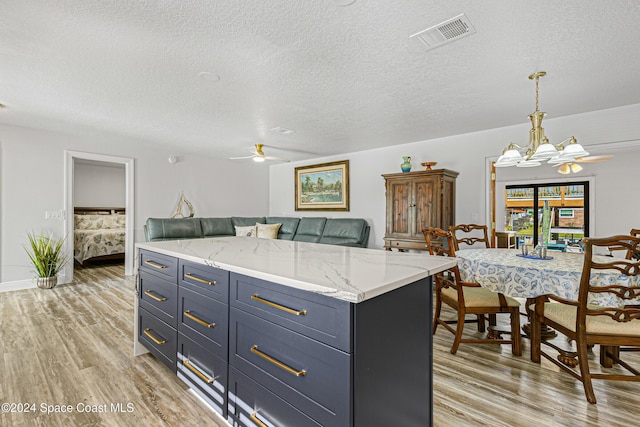 kitchen with hanging light fixtures, ceiling fan, light wood-type flooring, a textured ceiling, and a kitchen island