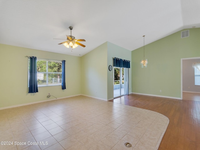 spare room featuring ceiling fan with notable chandelier, light wood-type flooring, and vaulted ceiling