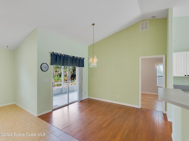 empty room with a chandelier, lofted ceiling, and light wood-type flooring