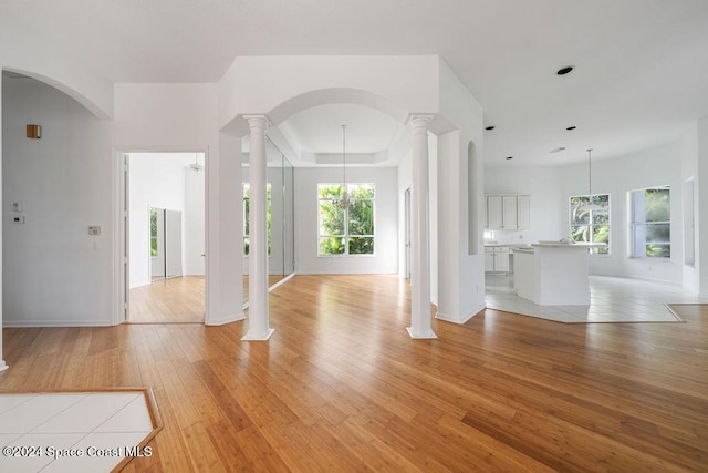 unfurnished living room with a tray ceiling, light hardwood / wood-style flooring, a notable chandelier, and ornate columns