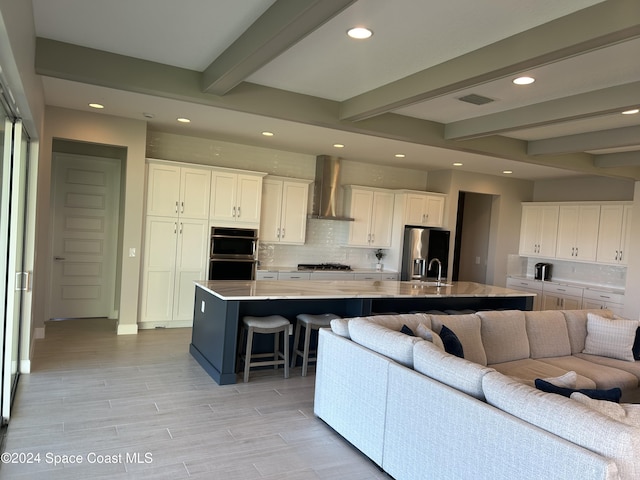 kitchen featuring a kitchen bar, white cabinets, wall chimney exhaust hood, beamed ceiling, and a large island