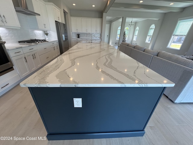 kitchen with wall chimney range hood, appliances with stainless steel finishes, a large island, light stone counters, and white cabinetry