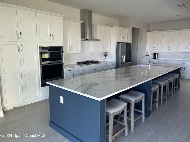 kitchen with a large island with sink, white cabinetry, wall chimney exhaust hood, and sink