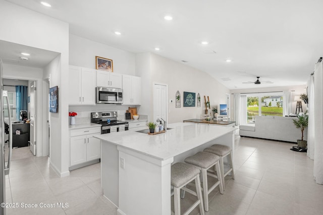 kitchen with light stone counters, stainless steel appliances, a kitchen island with sink, white cabinetry, and lofted ceiling