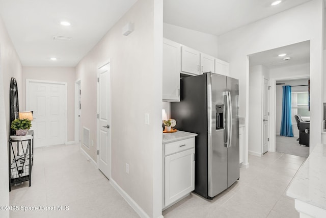 kitchen featuring lofted ceiling, stainless steel refrigerator with ice dispenser, light tile patterned flooring, light stone counters, and white cabinetry