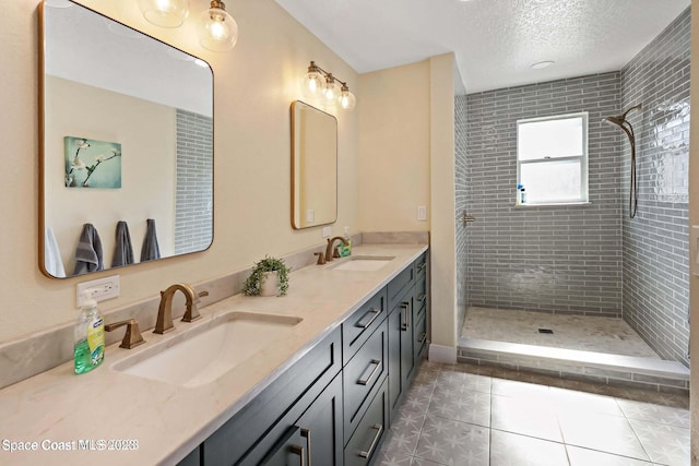 bathroom with tile patterned flooring, vanity, a textured ceiling, and tiled shower