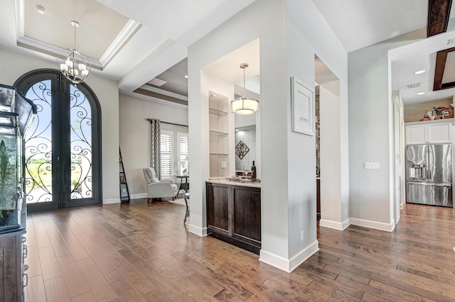 entryway featuring a tray ceiling, french doors, dark hardwood / wood-style floors, and a notable chandelier