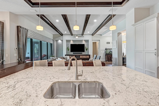 kitchen featuring pendant lighting, sink, ceiling fan, light stone countertops, and beamed ceiling