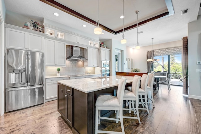 kitchen featuring white cabinetry, sink, wall chimney exhaust hood, stainless steel fridge with ice dispenser, and pendant lighting