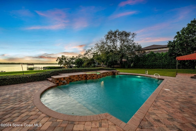 pool at dusk with a patio area, pool water feature, a yard, and a water view