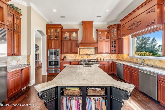 kitchen featuring light stone countertops, sink, built in appliances, a center island with sink, and custom range hood