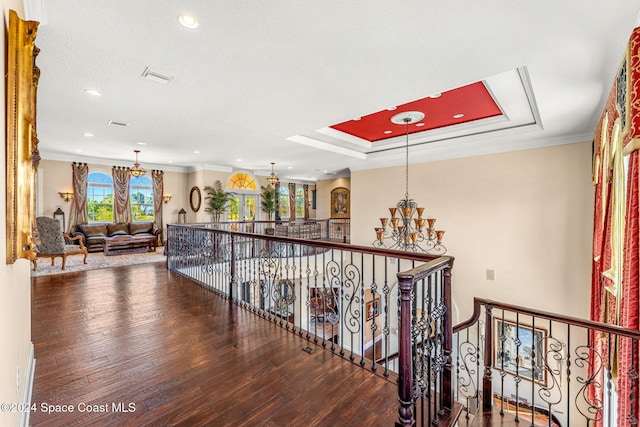 corridor with hardwood / wood-style floors, ornamental molding, a textured ceiling, a tray ceiling, and a chandelier