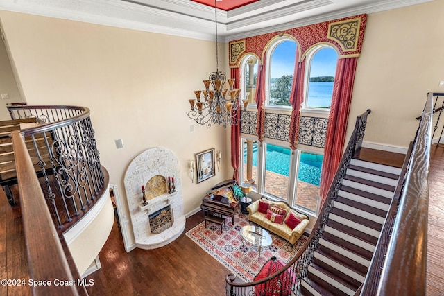 living room featuring a tray ceiling, crown molding, wood-type flooring, a water view, and an inviting chandelier